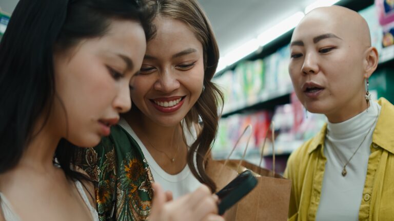 Asian women group shopping groceries, discussing content on a mobile phone