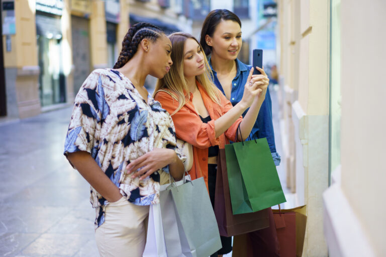 Multiracial women with shopping bags taking photo of showcase